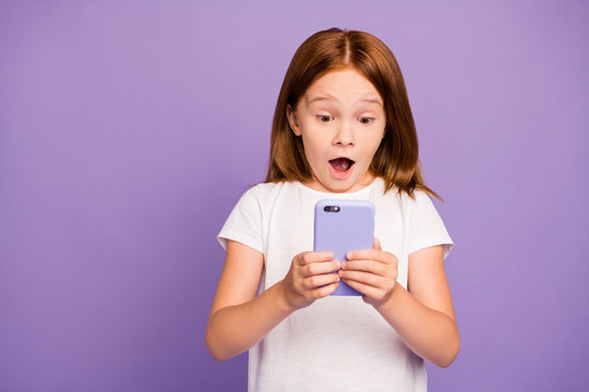 Photo of pretty little ginger lady holding telephone hands checking own children blog excited with many new followers wear white t-shirt isolated purple background