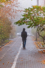 Morning fog in town in the fall. A man walks along the alley.