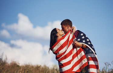 Kissing each other. Feels freedom. Beautiful couple with American Flag have a good time outdoors in the field