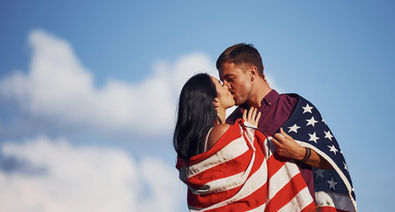 Kissing each other. Feels freedom. Beautiful couple with American Flag have a good time outdoors in the field