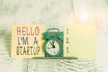 Writing note showing Hello I M A Startup. Business concept for Entrepreneur starting business Presenting New project Mini blue alarm clock standing above buffer wire between two paper