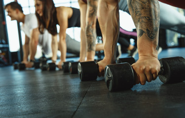 A group of muscular athletes doing workout at the gym. Gymnastics, training, fitness workout flexibility. Active and healthy lifestyle, youth, bodybuilding. Close up of hands with weights training.