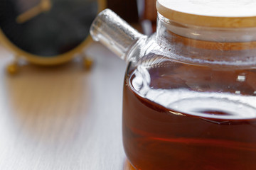Glass tea pot with black tea on wooden table