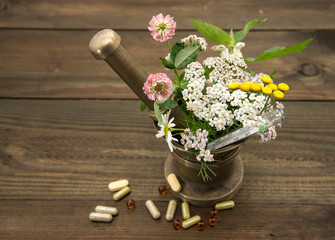 Herbs and a thermometer in a copper mortar and pestle, capsules and pills scattered around.