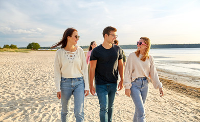 friendship, leisure and people concept - group of happy friends walking along beach in summer