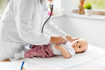 medicine, healthcare and pediatrics concept - close up of female doctor with stethoscope listening to baby girl's patient heartbeat or breath at clinic or hospital