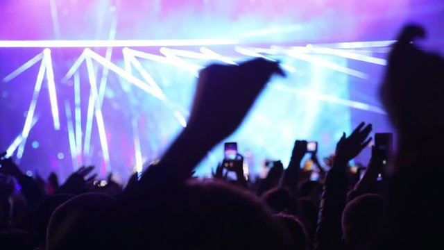 People cheer move lift and clap their hands in unison against the strobing stage lights. Young people lifestyle and nightlife. Laser show on live music concert. Handheld live video footage.