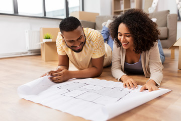 mortgage, people and real estate concept - happy african american couple with boxes and blueprint...