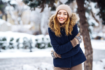 Beautiful  woman stands among snowy trees in winter forest. Young  girl dressed in a blue jacket...