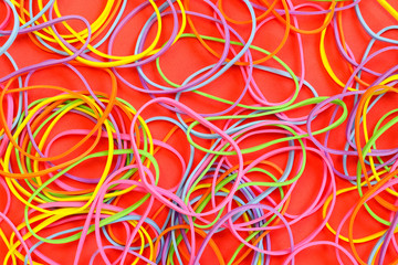 A pile of neon colored elastic rubber bands against a red background