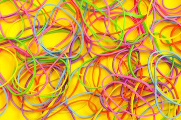 A pile of neon colored elastic rubber bands against a yellow background
