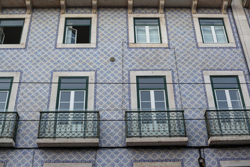 Fototapeta na wymiar A beautiful architecture of the traditional tiled walled facade with large glass doors and windows and the iron balcony in the city of Lisbon in Portugal
