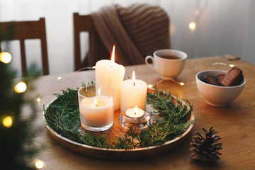 Cozy evening tea party by candlelight. Served table: cup of tea, cookies, tray, candles, pine cone,...