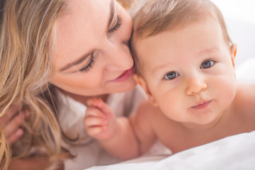 Mother and baby boy son playing on a white bed. Mothers tenderness and kisses of a toddler child