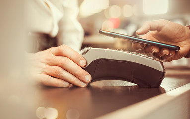 Customer hand pays with smartphone in store using NFC technology.  Mobile phone paying the bill...