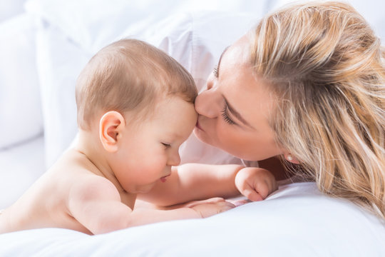 Mother and baby boy son playing on a white bed. Mothers tenderness and kisses of a toddler child