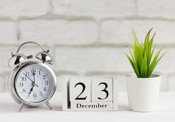 calendar from white wooden cubes and an alarm clock on the table 23 December on yard