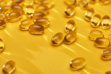 close up view of golden shiny fish oil capsules scattered on yellow bright background