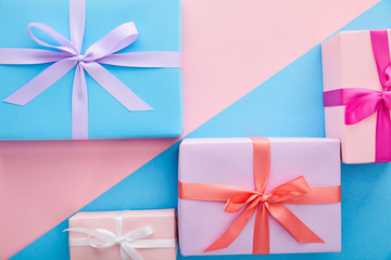 top view of colorful gift boxes with ribbons and bows on blue and pink background