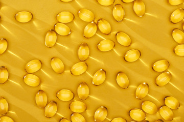 top view of golden shiny fish oil capsules scattered on yellow bright background