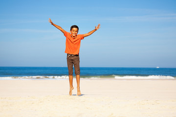 Fototapeta na wymiar Happy boy jump up with spread hands over sea beach