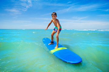 Little boy surfing sea waves standing on surfboard