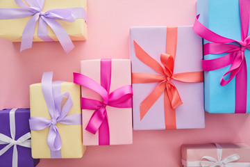 flat lay with colorful gift boxes with ribbons and bows scattered on pink background