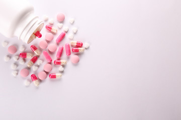Flat lay composition with bunch of different colorful pills scattered from the bottle over the table. Pile of opened medication on paper textured background. Close up, copy space.