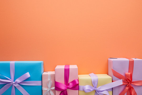 flat lay with multicolored gift boxes with ribbons and bows on orange background with copy space