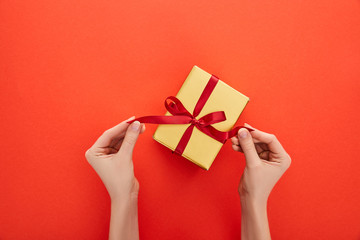 cropped view of woman untying ribbon on golden gift box on red background