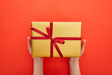 cropped view of woman holding golden gift box on red background