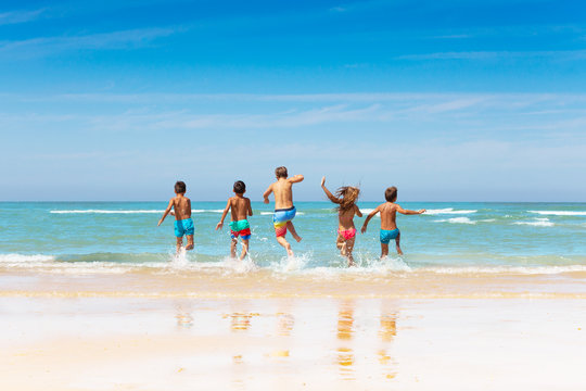 Many kids friends run into sea waves on sand beach