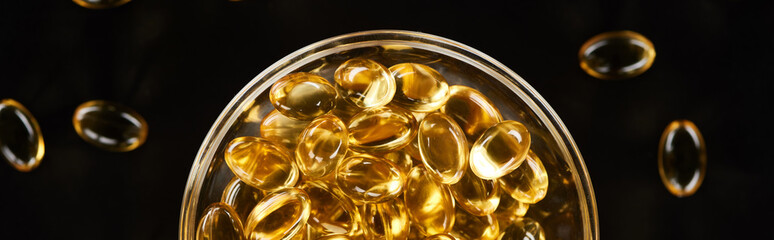top view of golden fish oil capsules in glass bowl isolated on black, panoramic shot