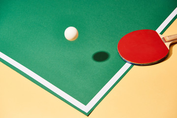Red table tennis racket and ball on paying table and yellow surface - obrazy, fototapety, plakaty