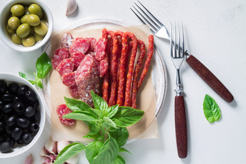 Set of chorizo sausages with olives and a sprig of basil. Antipasti snack