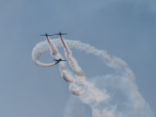 Three aircraft perform aerobatics, behind them stretches clearly visible against the blue sky inversion trail indicating the flight path.