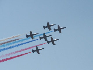 Six aircraft perform aerobatics, behind them stretches clearly visible against the blue sky trail of signal smoke, indicating the flight path.