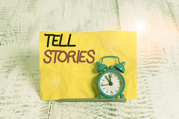 Word writing text Tell Stories. Business photo showcasing formal to tell someone about something that has happened Mini blue alarm clock stand tilted above buffer wire in front of notepaper
