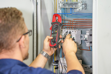 Electrician man measures voltage with multimeter in electrical cabinet. An electrician is checking...