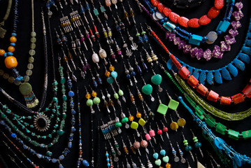Colorful dangly earrings and necklaces hang from a black board at an outdoor flea market