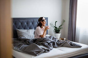 good morning concept - portrait of beautiful woman in pajamas sitting on bed and drinking coffee