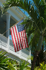 American flag hanging  from white railing patio of colonial house with palm tree accent in Key West