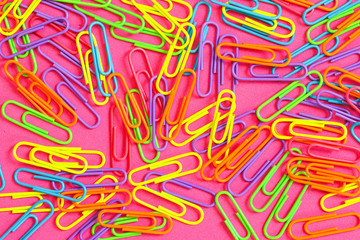 An assortment of brightly colored neon paperclips against a pink background