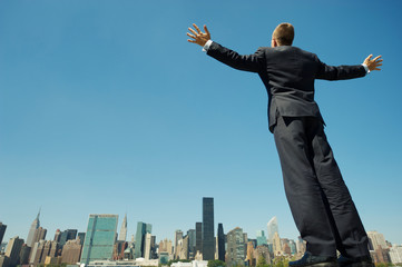 Fototapeta na wymiar Full length view of powerful businessman standing tall with his arms spread above the city skyline under bright blue sky copy space