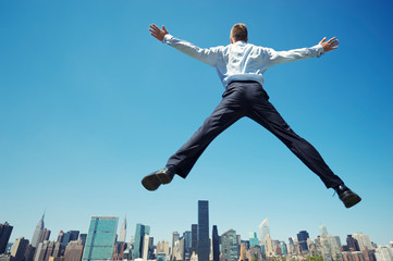 Fototapeta na wymiar Giant businessman doing a spreadeagle jump outdoors in a blue sky celebration above the city skyline