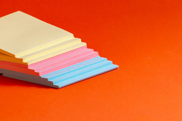 Obraz premium Multicolored sheets of office paper laid out in the shape of a staircase on an isolated, bright, orange background. Selective focus.