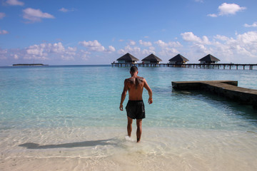 Fototapeta na wymiar man with a tattooed back walking towards the beach of a luxury resort in maldives