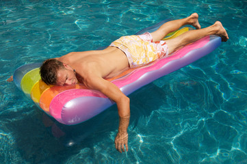 Man relaxing on a colorful inflatable lilo raft floating in a sunny swimming pool