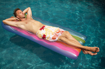 Man relaxing on a colorful inflatable lilo raft floating in a sunny swimming pool
