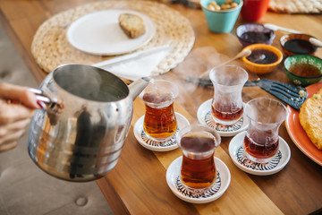 Pouring tea from tea pot to glass. Breakfast preparation concept. Traditional Turkish brewed tea drink in morning also as known "Cay" or "Turk Cayi". Relaxing or resting mood, break time concept.